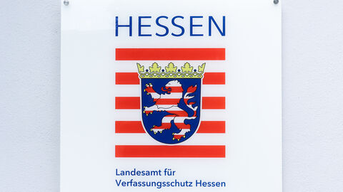 Ein weißes Türschild mit dem Wappen des Landes Hessen und der Aufschrift Landesamt für Verfassungsschutz in blauer Schrift