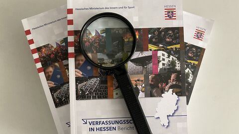 Drei Jahresberichte des LfV Hessen übereinander gelegt. Auf dem obersten Bericht liegt eine Lupe. Drei Jahresberichte des LfV Hessen übereinander gelegt. Auf dem obersten Bericht liegt eine Lupe.