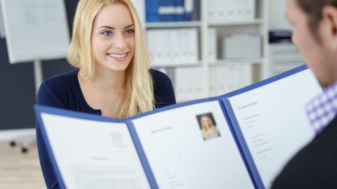 Junge Frau beim Bewerbungsgespräch Bewerbungsgespräch - Zwei Menschen sitzen sich gegenüber, wobei eine Person eine Bewerbungsmappe hält