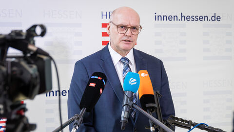 LfV-Präsident Bernd Neumann steht vor einer Pressewand, wird von einer Kamera aufgezeichnet und spricht in mehrere Mikrofone.