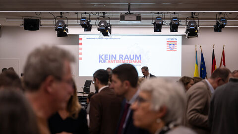 Blick in den Veranstaltungssaal. Auf eine Leinwand wird der Satz "Kein Raum für Extremismus projiziert